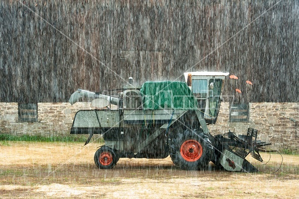 Combine harvester sitting in barn yard during rain storm. 
