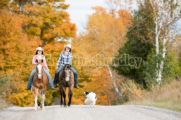 Two young women horseback riding through autumn colored scenery