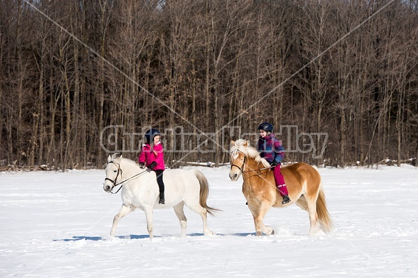 Two young girls riding their ponies in the snow