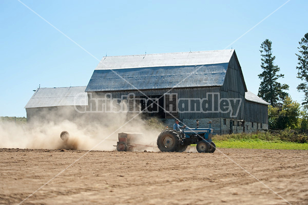 Farmer driving tractor and seed drill seeding oats