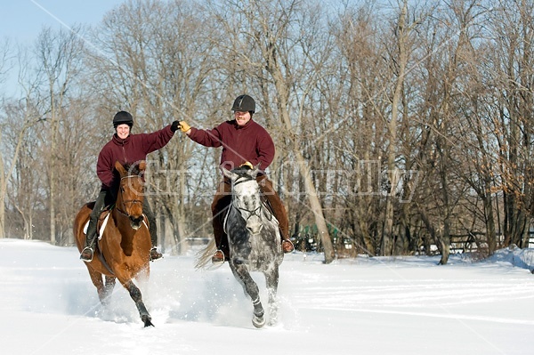 Husband and wife horseback riding through the deep snow holding hands