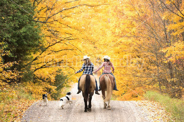 Two young women horseback riding through autumn colored scenery