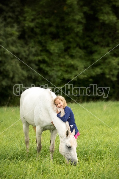 Portrait of a young girl hugging a gray pony in a field