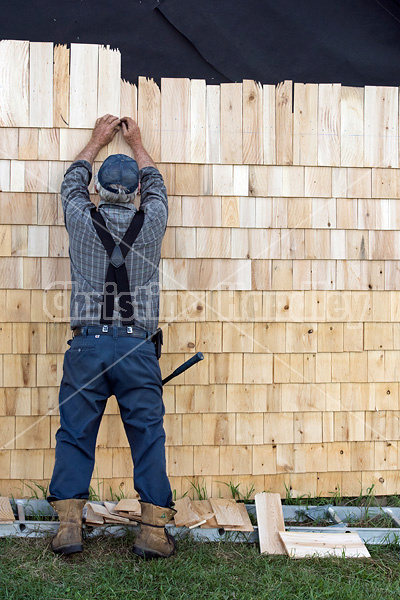 Man putting cedar shingles on the wall of a barn