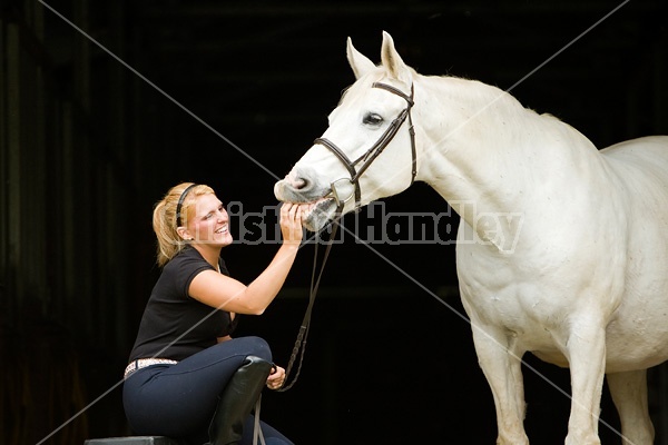 Young woman and white horse posing in barn doorway with black background