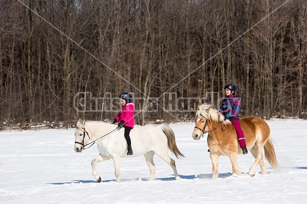 Two young girls riding their ponies in the snow
