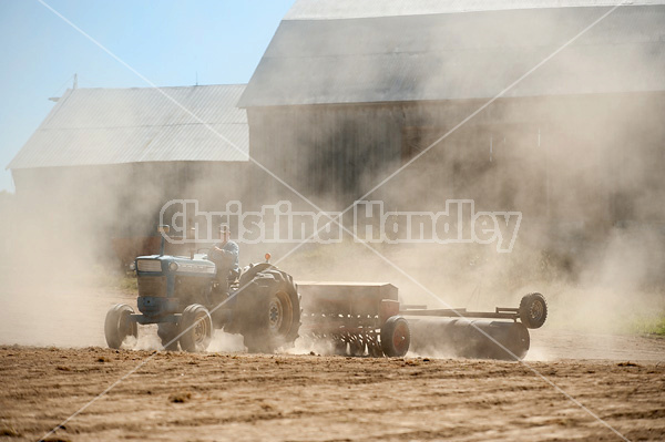 Farmer driving tractor and seed drill seeding oats