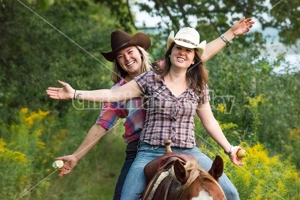 Two young women riding double in a western saddle