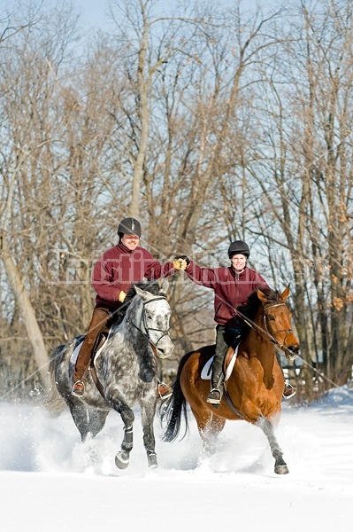 Husband and wife horseback riding through the deep snow holding hands