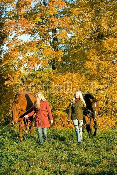 Two women leading horses through field.