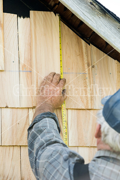 Man putting cedar shingles on the wall of a barn