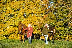 Two women leading horses through field.