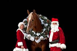 Santa Claus and Mrs Claus standing with a Belgian draft horse with a Christmas wreath over its head.