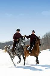 Husband and wife horseback riding through the deep snow holding hands
