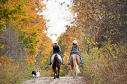 Two young women horseback riding through autumn colored scenery