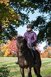 Woman horseback riding in field in the autumn of the year with colored leaves in the background