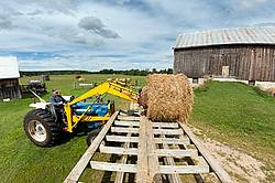Farmer unloading round bales of straw from hay wagon with a front end loader tractor