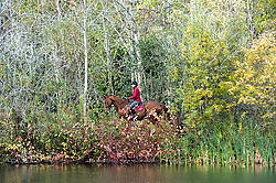 Woman horseback riding around pond in the autumn colors