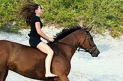 Young woman riding a hrose bareback in the sand