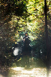 Woman horseback riding through a cedar forest in the autumn time