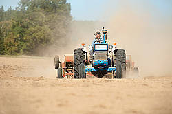 Farmer driving tractor and seed drill seeding oats