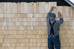 Man putting cedar shingles on the wall of a barn