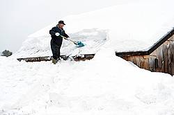Man shoveling heavy snow off barn roof.