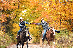 Two young women horseback riding through autumn colored scenery