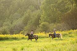 Two young women horseback riding western on a summer evening