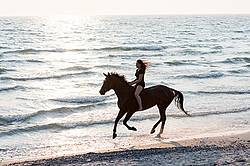 Young woman horseback riding in the surf of Lake Ontario. 