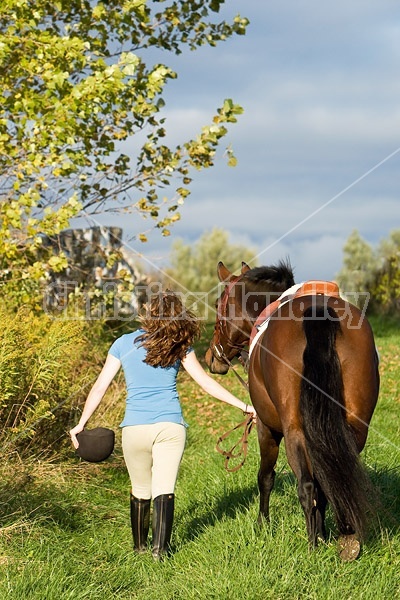 Young woman walking her horse on a grass path